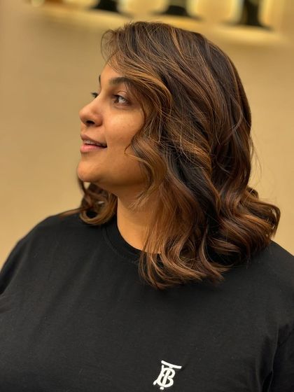 A side view of a client with creative, warm-toned color. The soft waves and rich shades create a unique and stylish look that stands out.