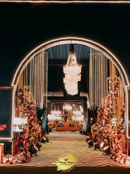 A radiant entrance for a night of glamour. This arched gateway, illuminated with warm lights and flanked by intricate decor panels, sets a sophisticated tone for an unforgettable cocktail or sangeet evening.