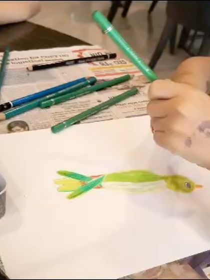 A close-up of a student using colored pencils to draw a parrot, carefully layering greens to create texture and depth.