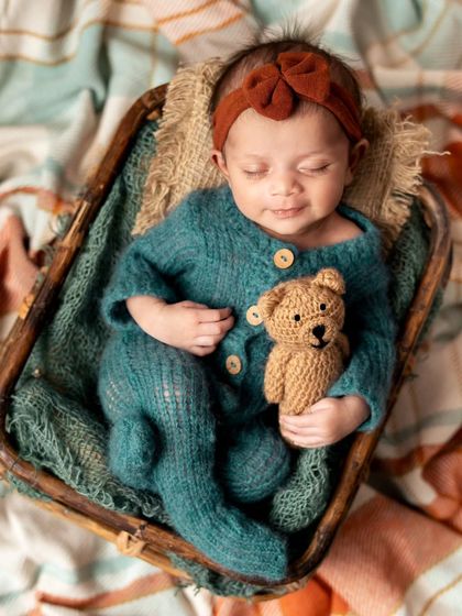 A sweet newborn girl in a cozy knit outfit, cuddling her tiny teddy bear. I have a variety of adorable outfits and props to add a touch of personality to your session.
