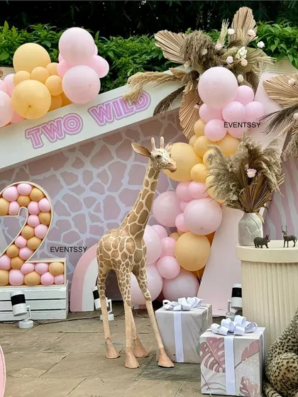 A detail shot from the "Two Wild" party, focusing on the giraffe prop and the balloon-filled marquee number "2." The giraffe-print backdrop adds another layer of texture to the design.