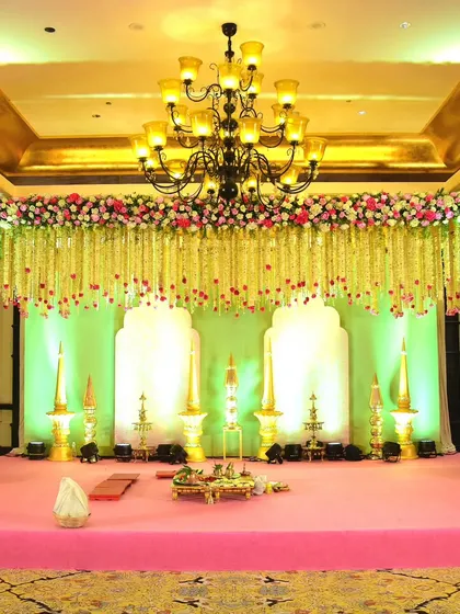 A wide shot of the traditional South Indian mandap, showing the beautiful contrast of the pink stage, golden pillars, and the canopy of white and pink floral garlands.