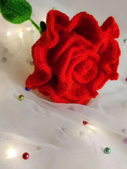 The crochet rose placed on a delicate white fabric with scattered beads, creating a dreamy, romantic feel.