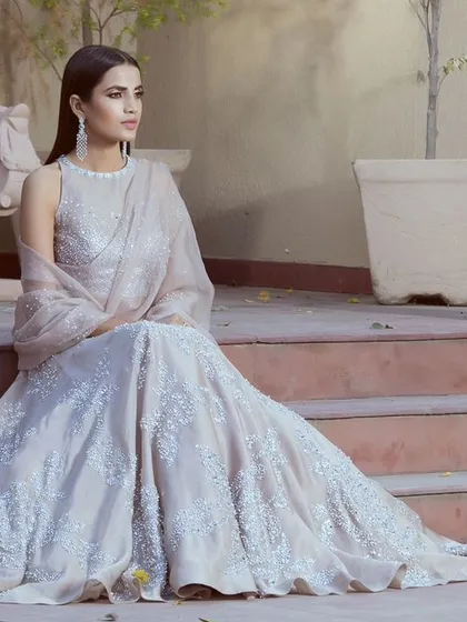 A wider shot from the same designer campaign, showing the full silhouette of the embroidered gown. The setting adds a touch of architectural elegance, providing context and a sense of luxury to the ethnic wear.