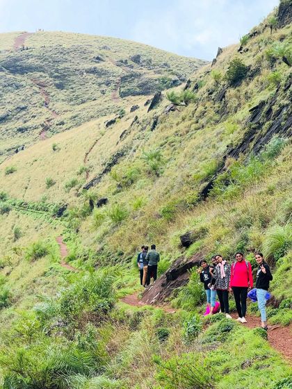 Trekkers on the path, with the steep green slopes of a Chikmagalur hill beside them.