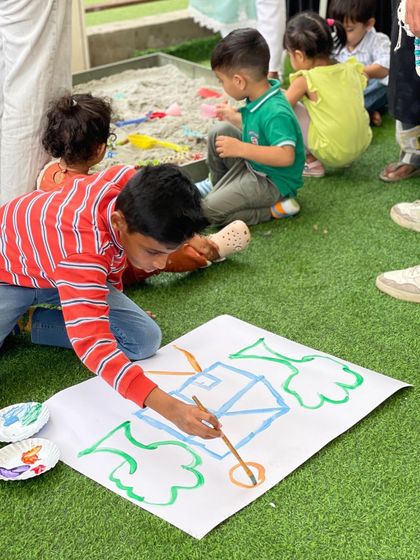 I love providing a space for unstructured creativity. This young artist is painting freely on a large canvas, while others in the background enjoy the sand pit. It’s all about joyful, messy, and memorable play.