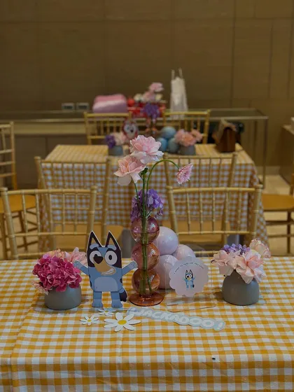 The adults' table at the Bluey party, featuring a yellow gingham tablecloth and beautiful pink and purple floral arrangements.