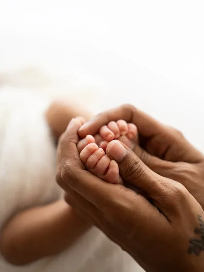 A close-up of a mother's hands holding her baby's feet. The tattoo on her wrist adds a personal and modern touch to this classic shot.