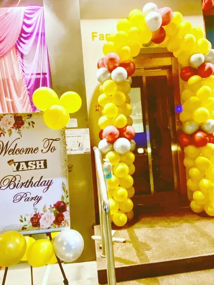 The entrance to the party venue, decorated with a yellow, red, and white balloon arch.