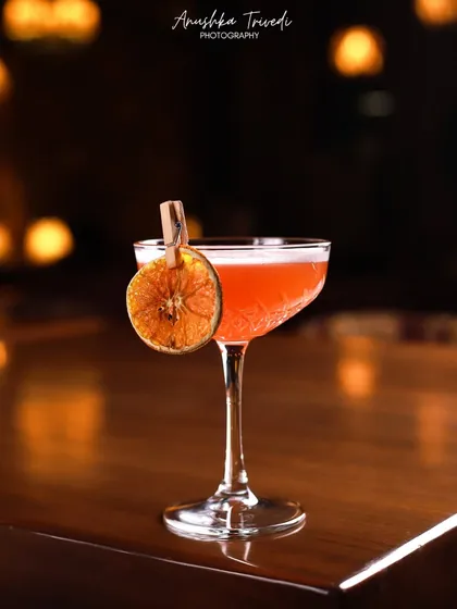 A beautiful cocktail glowing in the warm, ambient light of a bar. The bokeh effect from the lights in the background creates a sophisticated and intimate mood.