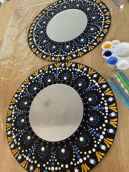 Two completed mandala mirrors on a table, showing the beautiful blue, yellow, and white dot patterns.