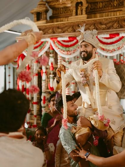 The groom being joyfully lifted by his friends and family during the garland exchange ceremony, a fun and competitive ritual.