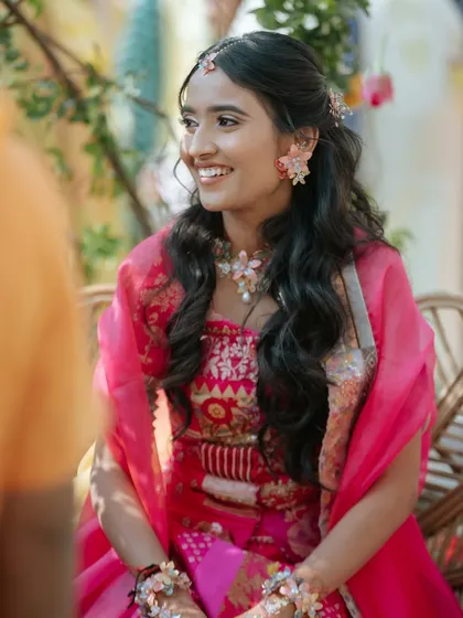 A candid photo of a bride at her Haldi ceremony. Her hair is styled in a simple half-updo with loose waves, giving her a natural and radiant look.