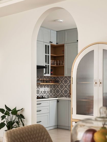 An archway provides a beautiful frame for the view into the kitchen, where another arched cabinet is visible, creating a sense of design cohesion.