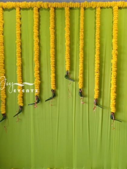 A simple and charming background decoration for a mature function. This design uses a lime green backdrop framed with yellow marigolds, with hanging parrot motifs that add a playful element.