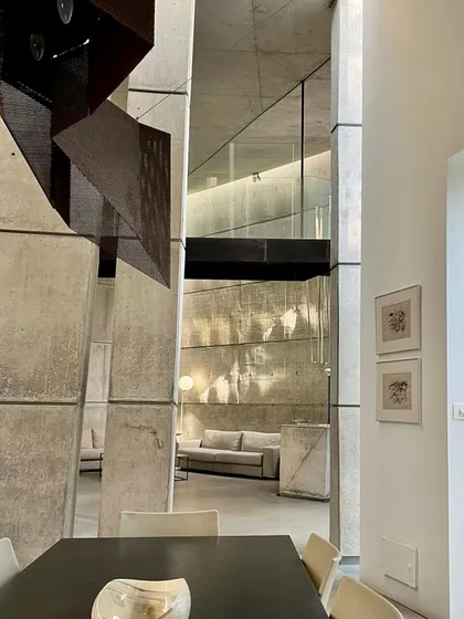 An interior view of the 'House of Stories', where light from an unseen source grazes a tall concrete wall. The way light interacts with the raw texture of the material is a central theme of this home's design.