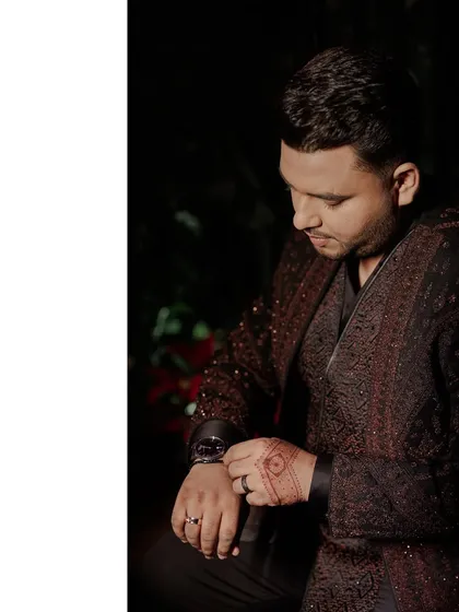 A close-up of the groom adjusting his watch. This shot focuses on the details of his outfit, including the intricate pattern of his jacket and the henna on his hand.