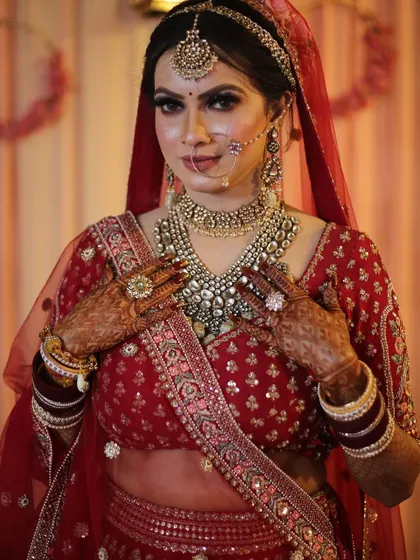 The bride admiring her stunning layered necklace, a perfect choice for her traditional red lehenga.