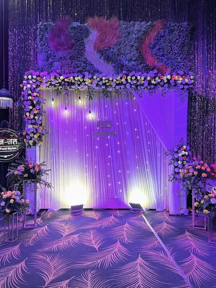 A stunning photo backdrop for a 25th-anniversary party, featuring a wall of greenery, a shimmering curtain, and dramatic purple uplighting.