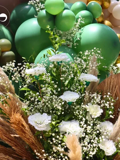 A beautiful floral arrangement combining pampas grass, white carnations, and baby's breath against a backdrop of green balloons. This decor element was part of a tranquil green and white Godh Bharai.