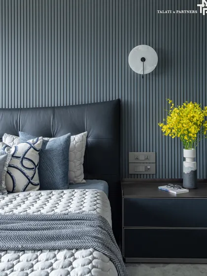 A detail of the bedroom, showing the deep blue fluted wall paneling and a leather headboard. A layered mix of high-end materials, including marble and plush textiles, defines the space, while fresh yellow flowers add a soft, personal touch.
