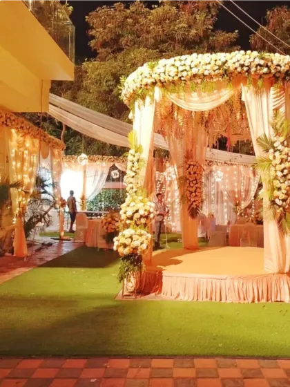 A beautiful mandap for an evening wedding on a lawn, decorated with peach drapes, white flowers, and fairy lights for a warm, glowing effect.
