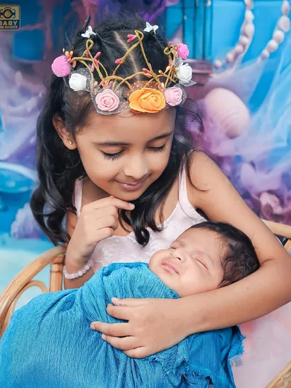 A close-up showing the gentle and loving gaze of a big sister looking at her sleeping newborn brother.