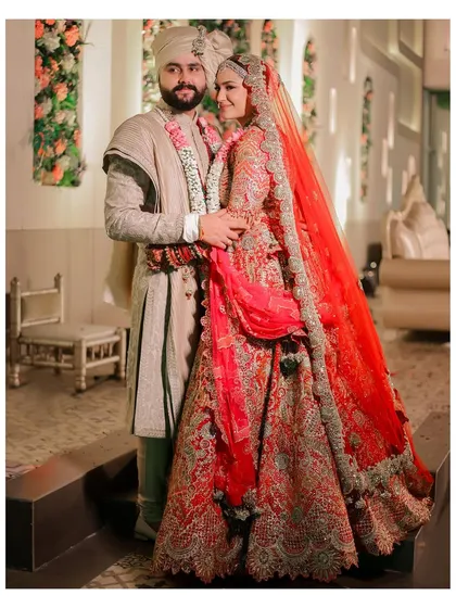 A classic wedding day portrait of the couple. The bride's stunning red lehenga and the groom's coordinated attire are captured in a moment of loving embrace.