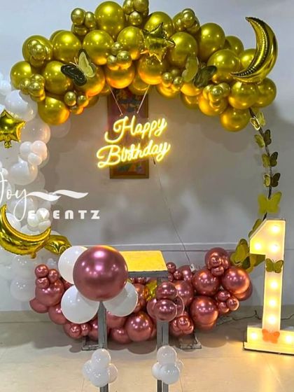 For this first birthday, I designed a celestial-themed balloon ring. The arch features white and gold balloons, accented with moon and star foil balloons and a 'Happy Birthday' neon sign.
