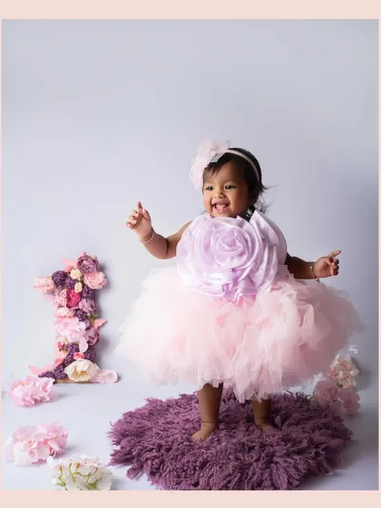 Standing tall and proud for her first birthday. This shot captures her excitement and the beautiful details of her floral-themed party dress.