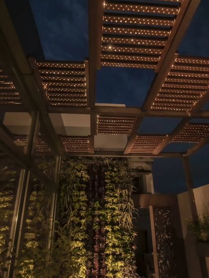 A Tipwood pergola with integrated lighting, creating a beautiful ambiance over a terrace with a vertical garden.