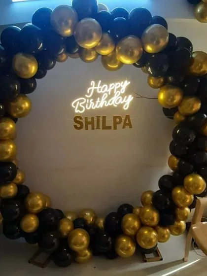 Celebrating in style with a chic and modern black and gold theme. This circular balloon arch is perfect for adult birthdays, anniversaries, or any sophisticated event. The custom neon sign with the name "Shilpa" adds a personal touch against the classic color combination.