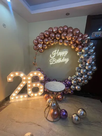This is a duplicate of ID 37, 80, 136, 139, 151, 203, 247. A stylish half-arch balloon ring for a 26th birthday. This home decoration uses chrome rose gold and silver balloons, a neon sign, and marquee numbers.