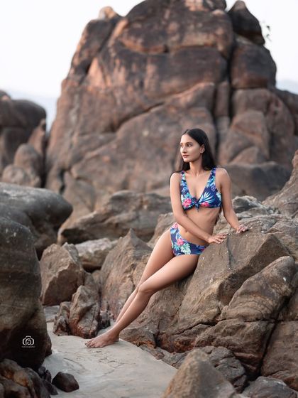 A relaxed pose in a floral bikini, with the model looking off to the side. The rocky beach provides a stunning and textured backdrop for this swimwear shot.