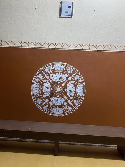 This is an Alpona mandala, a traditional folk art style. We painted two of these, as twin mandalas on adjacent walls, creating a striking and symmetrical feature with its bold white pattern on an earthy brown background.