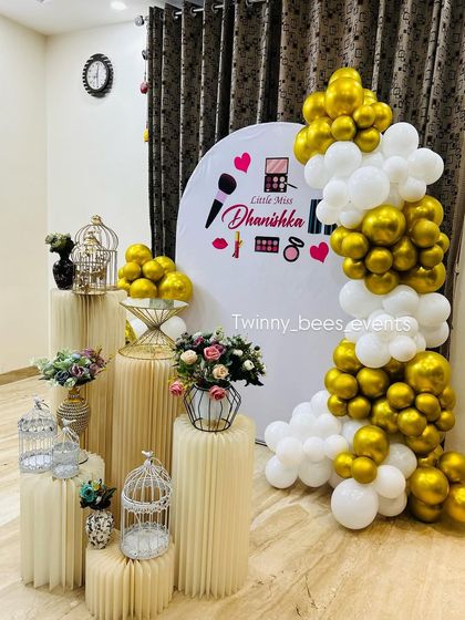 A different angle of the makeup-themed party for Dhanishka. This view showcases the elegant fluted pedestals and the stylish gold and white balloon garland that framed the custom backdrop.