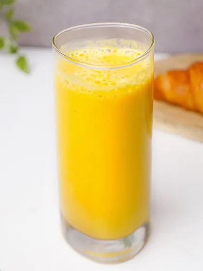 A tall glass of fresh mango smoothie, presented alongside a golden croissant in a bright, clean setting. This composition is perfect for a cafe's breakfast or beverage menu.