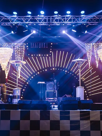 A retro-themed sangeet stage, complete with a checkered floor, sunburst lighting design, and cascading crystal chandeliers, ready for a night of music and dancing.