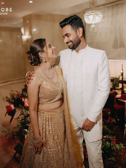 This couple shares a loving gaze during their shoot. He is dressed in a clean, all-white modern sherwani, which looks stunning against the warm, elegant backdrop.