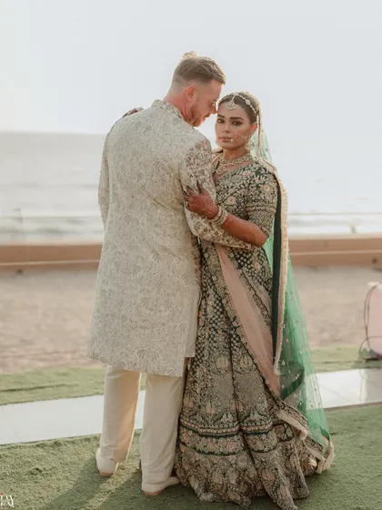 A powerful portrait from a cross-cultural beach wedding, where the bride looks confidently at the camera while the groom holds her close.