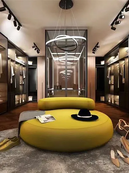 An expansive and luxurious walk-in closet featuring glass-paneled wardrobes with internal lighting, a central seating ottoman, and ample shelving. This custom closet design provides exceptional organization and a high-end boutique feel.