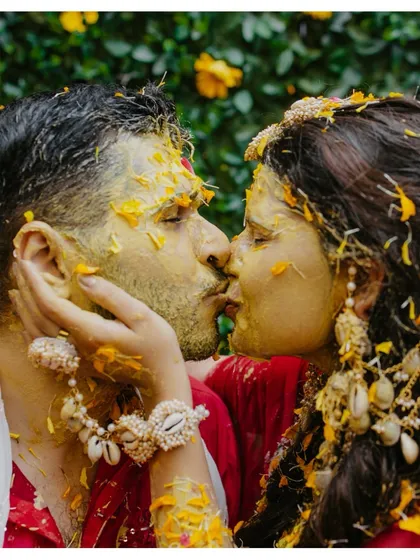 An intimate and playful kiss between the couple, their faces covered in turmeric and flower petals.