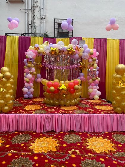 A clear, straight-on shot of the birthday stage inside the tent. The decor includes a 'Happy Birthday' banner, star and butterfly foil balloons, and pillars of golden balloons.