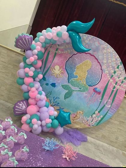 A close-up of a beautiful mermaid-themed backdrop. The circular board features an underwater scene with a mermaid silhouette, decorated with a cascade of pastel balloons and a mermaid tail.