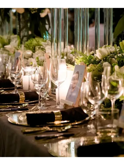 A close up of a sophisticated table setting for a formal birthday dinner. The combination of classic white and gold dinnerware, crystal glassware, and soft candlelight reflects our attention to detail in creating a refined ambiance.