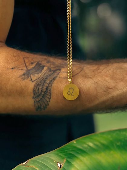 A gold round pendant with the Leo zodiac symbol, held to show the detail of the engraving. This is a great option for a personalized gift for the Leo in your life.