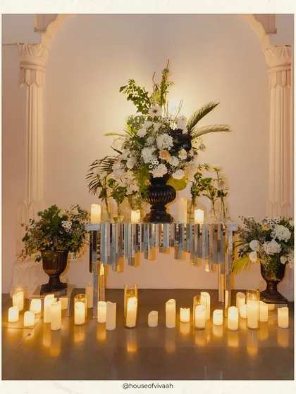 An elegant vignette with a floral arrangement on a mirrored console table, surrounded by a sea of candles, creating a moment of quiet glamour amidst the party.