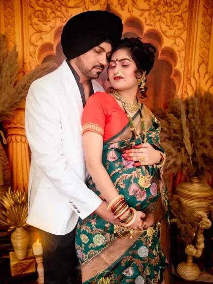 An intimate moment captured during a traditional maternity shoot. The couple shares a quiet, loving embrace, dressed in elegant ethnic wear against a richly decorated backdrop.