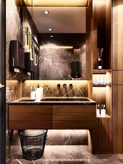 A look at a luxury commercial restroom where design continuity is key. We used dark marble, warm wood tones, and sophisticated lighting, including backlit mirrors and pendant lamps, to create a high-end experience for users.