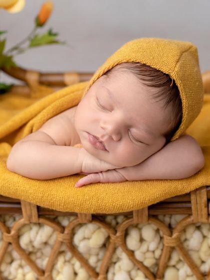 A pop of sunshine yellow. This newborn is sleeping peacefully on a rattan bed, bringing a bright and happy feel to the portrait.